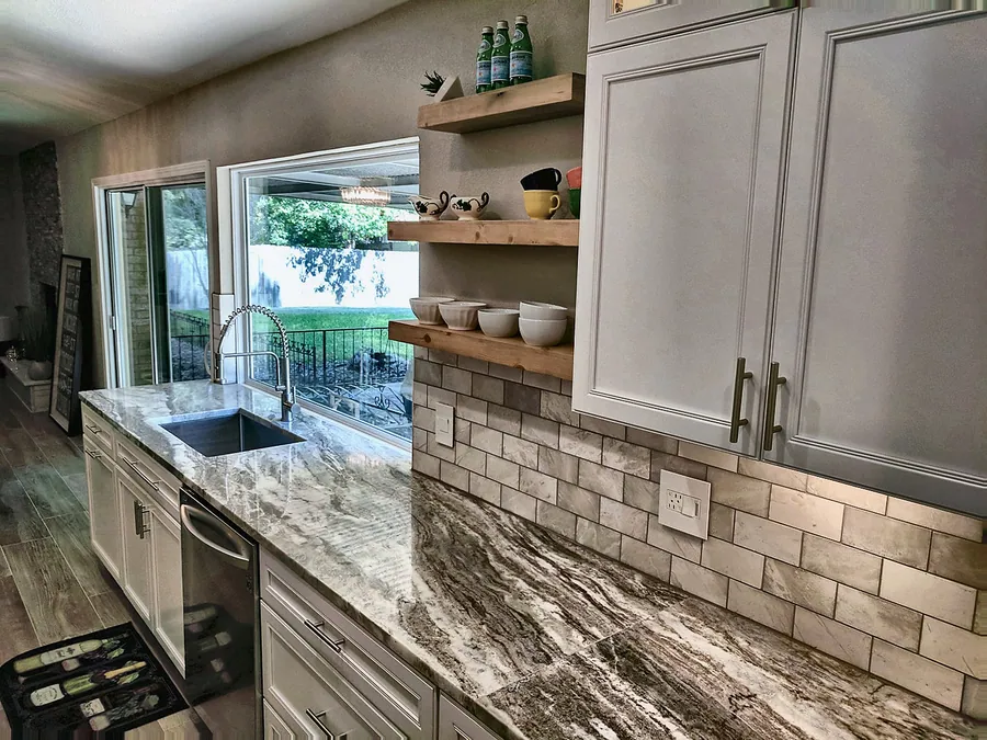 Light cabinetry and textured backsplash tile around a sink.