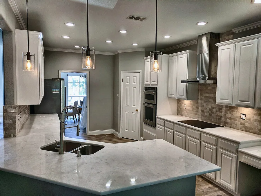 Bright kitchen with white cabinets, polished island and decorative pendant lights