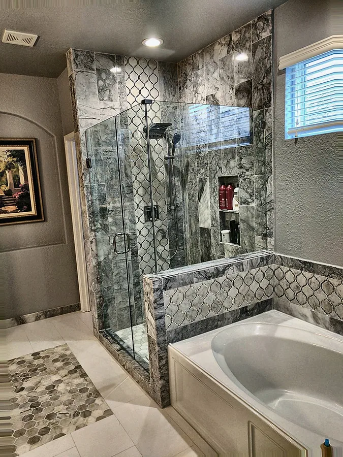 An updated bath featuring stone-look tile and glass shower panels.